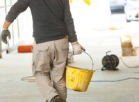 man holding a bucket on concrete contractor jobsite.