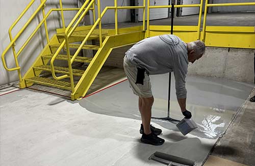 A man applying a coating to a concrete floor in an industrial facility.